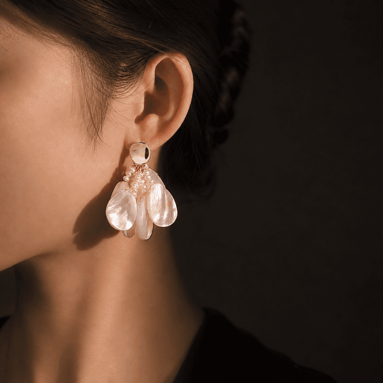 Model wearing shell-and-pearl drop earrings in warm studio light