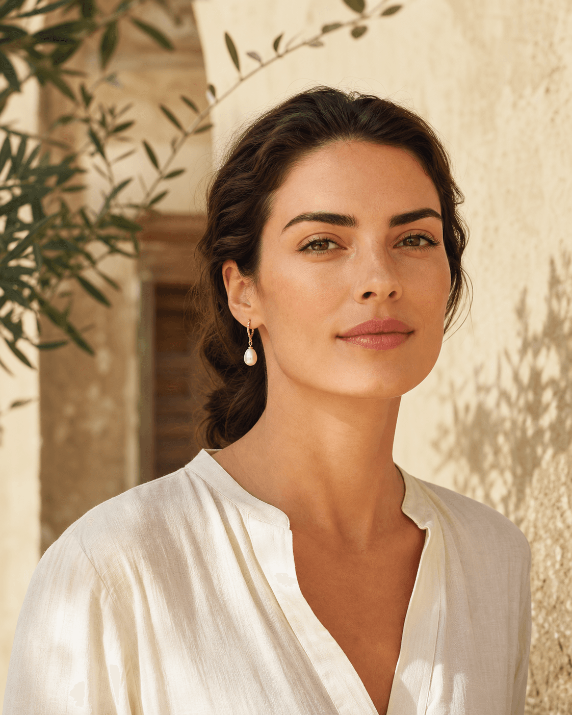 Model wearing pearl drop earrings in a sunlit limestone courtyard