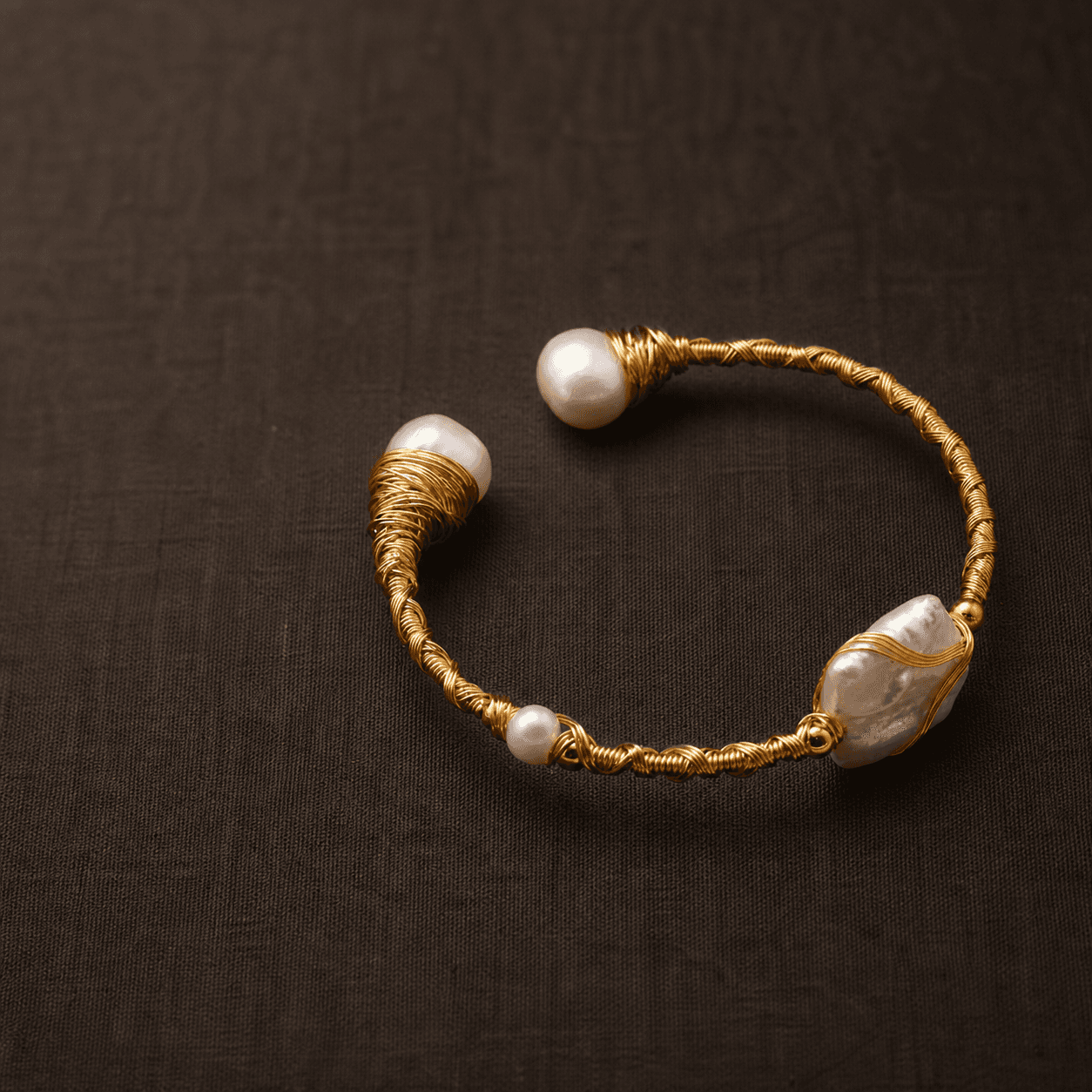 Gold wire pearl bracelet displayed on dark fabric